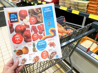 A person holding an ALDI ad while pushing a cart inside Aldi.