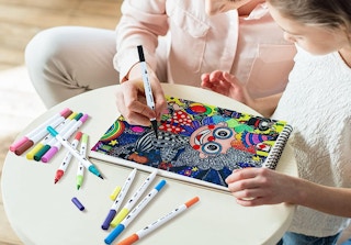 two people drawing with markers on in a sketch pad