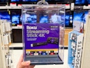 A Roku Streaming Stick 4k held out by hand in front of aisle.