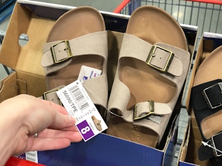 A person holding a price tag on a pair of sandals.