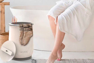 a woman sitting on the edge of a bathtub in a robe waiting for her towels to warm up in the Iconic Towel Warmer
