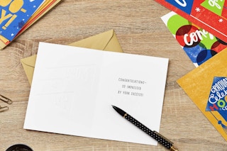 graduation cards laying on a wooden table with a pen