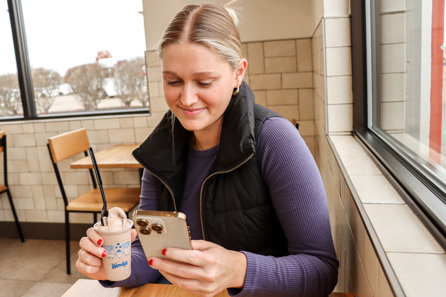 person looking at their phone inside of wendys while holding a frosty