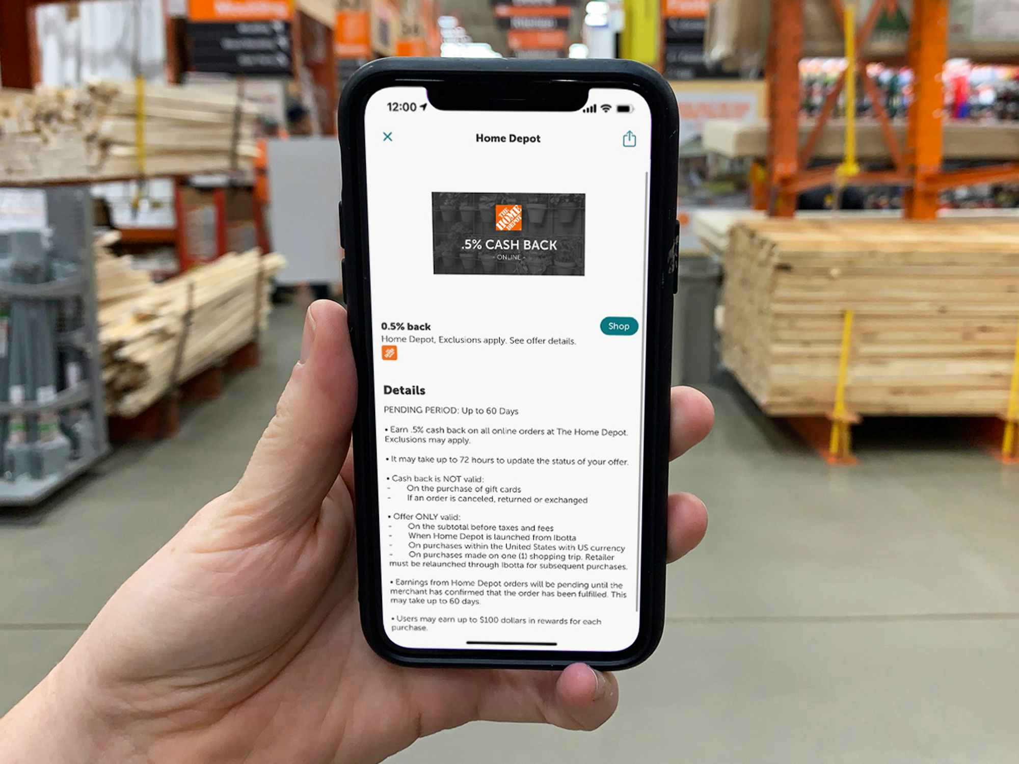 A person's hand holding up a phone displaying the Home Depot offer page on the Ibotta app inside Home Depot.