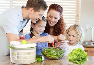family of four in the kitchen making a salad with salad spinner on the counter
