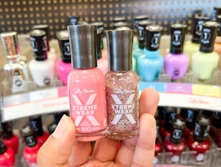 hand holding two Sally Hansen Xtreme Wear nail polishes in front of display of more nail polishes