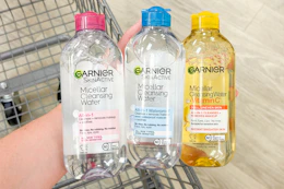 person holding 3 bottles of garnier micellar water over a cart