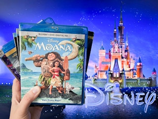 A person holding a stack of Disney blu-ray movies in front of a TV with the Disney logo on the screen
