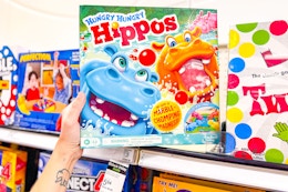 person grabbing a hungry hungry hippos board game off the shelf