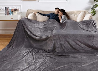 a couple on a couch with a big grey blanket 