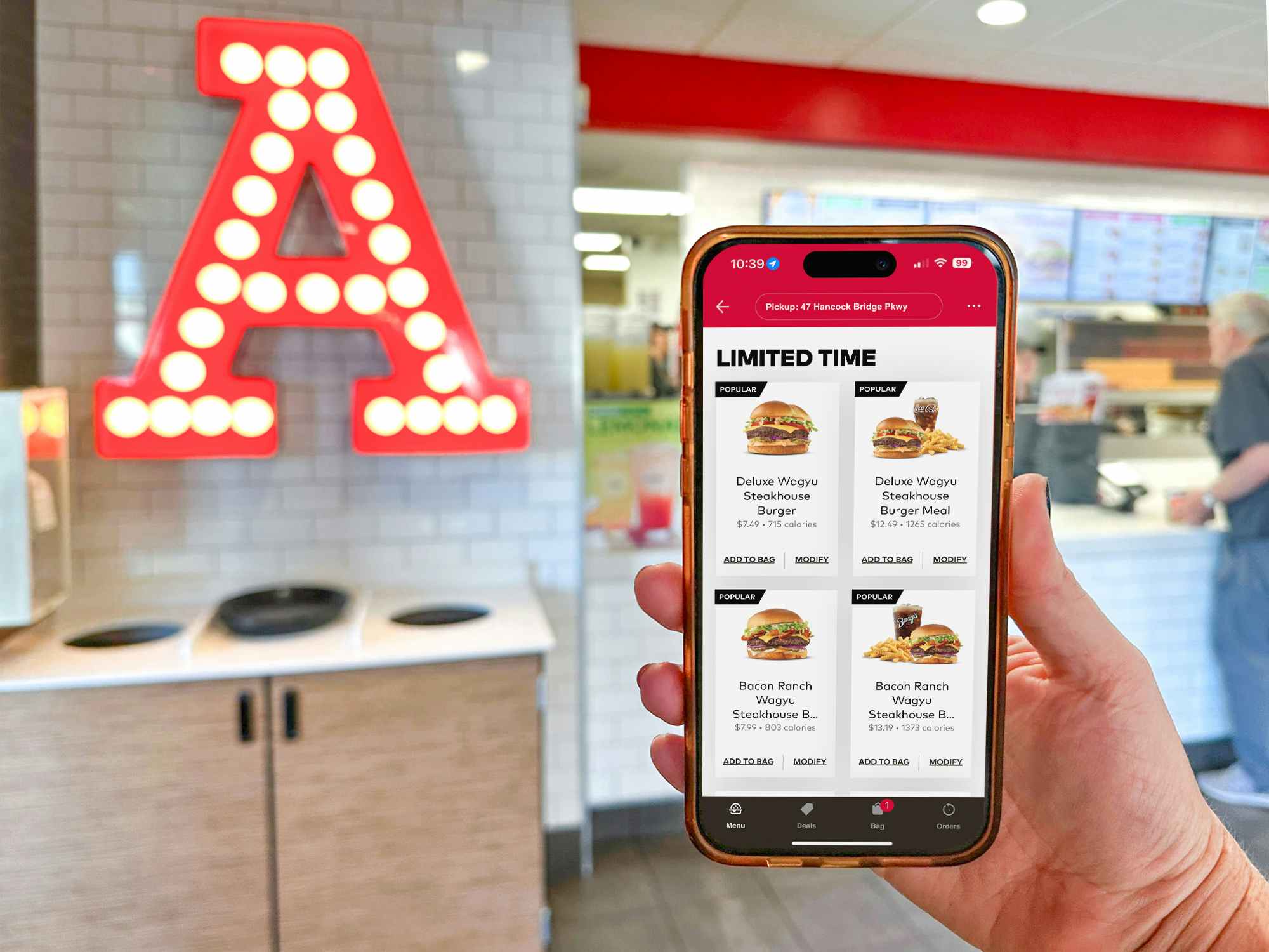Someone holding a phone displaying the Arby's app next to an Arby's sign