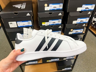 An Adidas Grand Court Mens Sneaker held out in front of several boxes of Adidas.