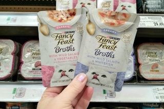 a hand holding two packs of of cat food