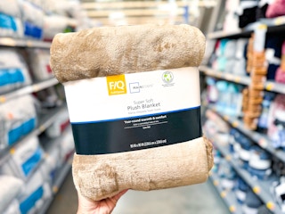 hand holding a queen size tan plush blanket in the bedding aisle of Walmart