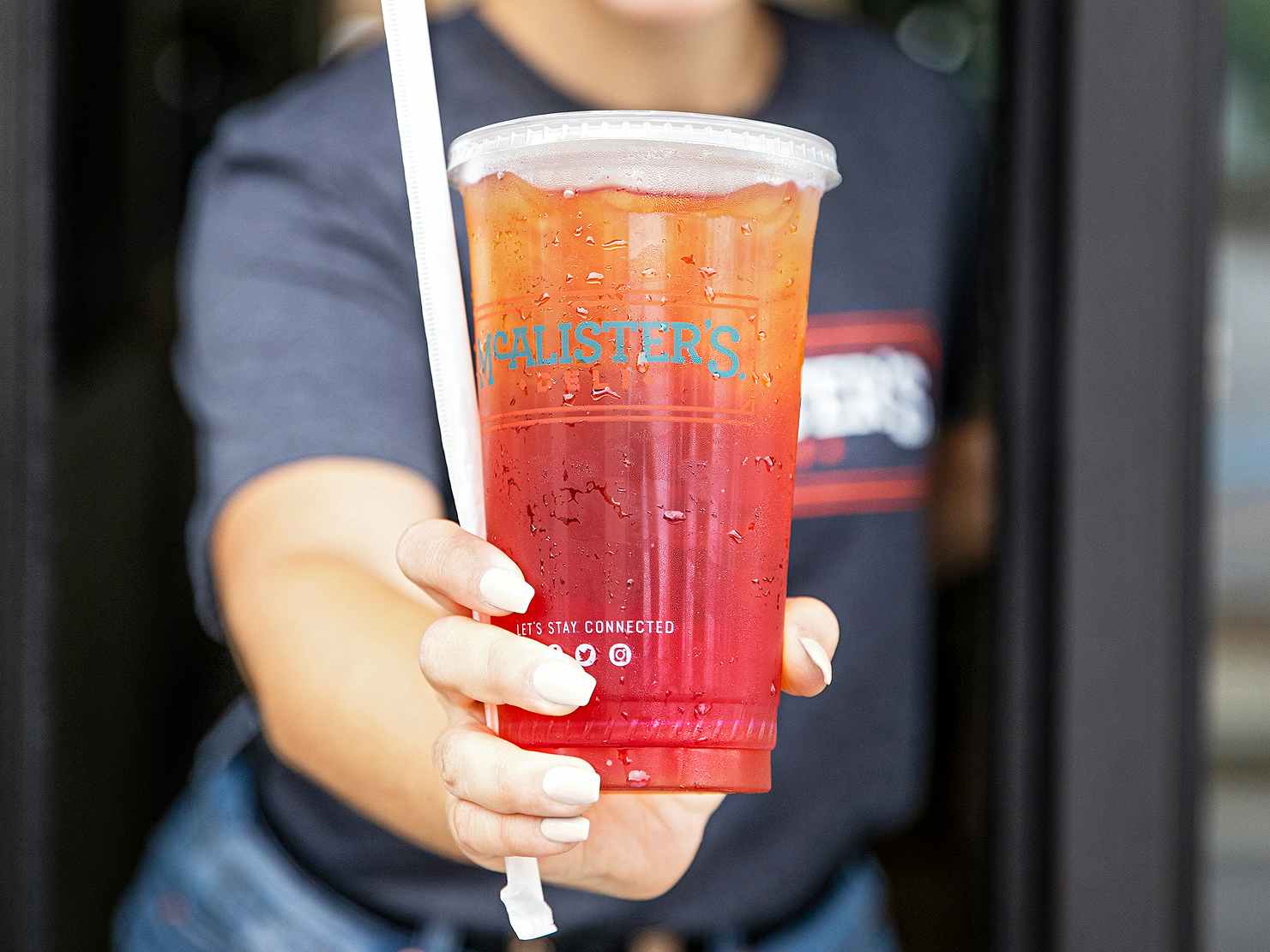 mcalisters deli employee handing an iced tea through the drive-through window