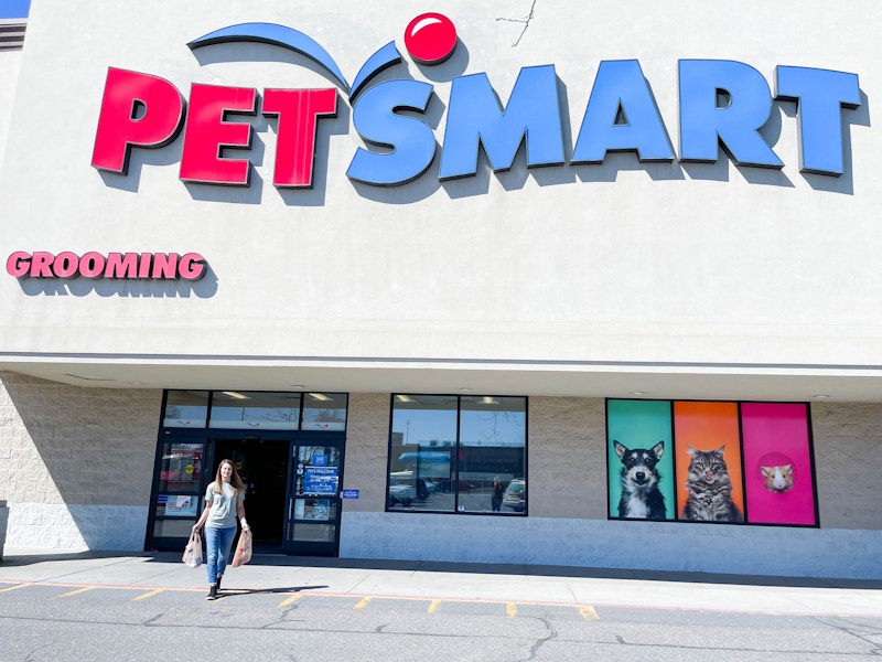 A woman carrying bags, walking out of a PetSmart storefront.