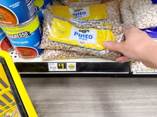 person grabbing a 16 ounce bag of dry pinto beans from a dollar general shelf for one dollar