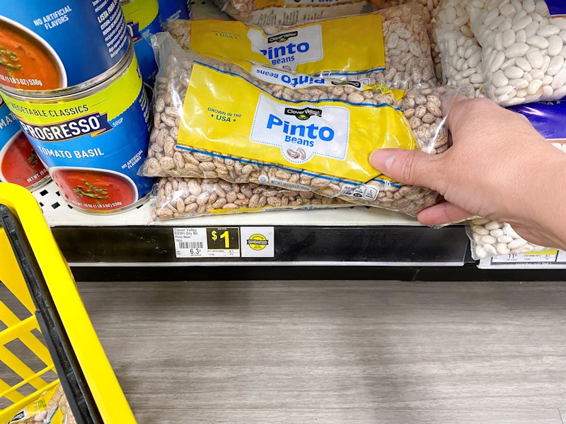 person grabbing a 16 ounce bag of dry pinto beans from a dollar general shelf for one dollar