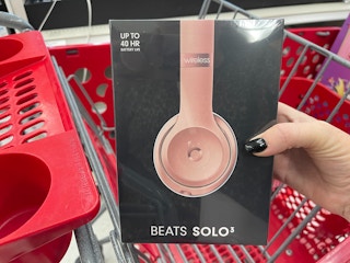 A person's hand holding a Beats Solo 3 box up in front of a Target shopping cart.