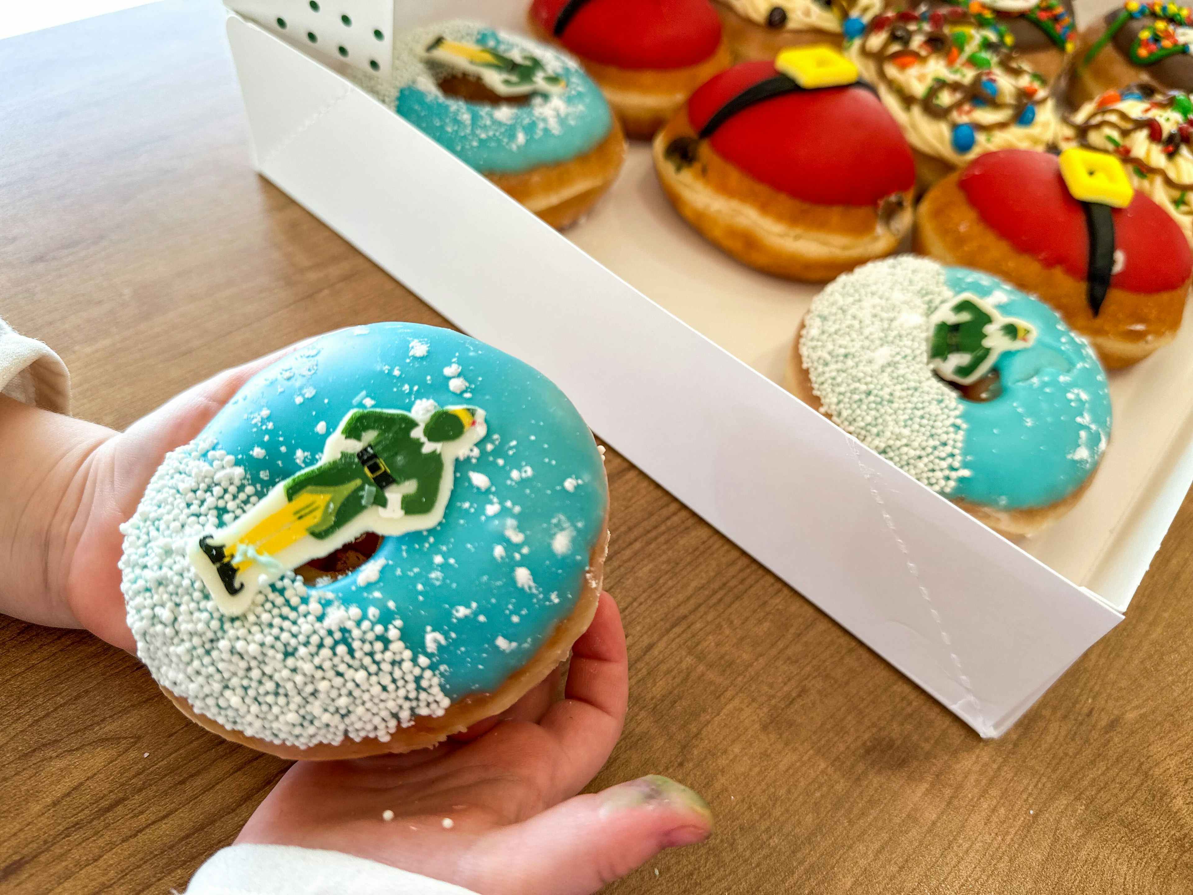 Hands holding a Elf Themed donuts from Krispy Kreme 