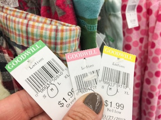 Someone holding up different colored Goodwill price tags in front of a rack of clothing