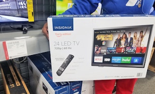 A person holding an Insignia TV in a store aisle.