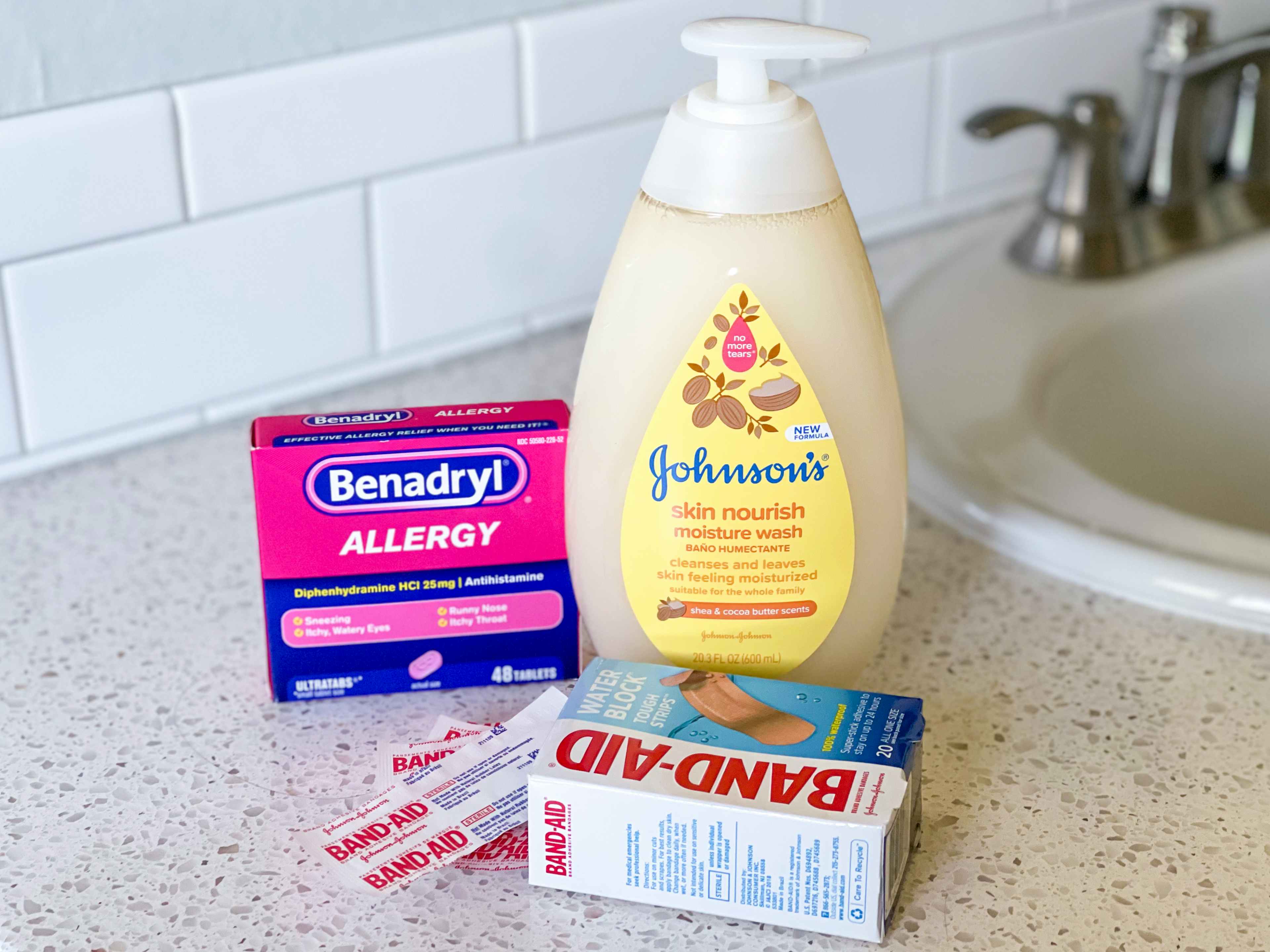 A box of Benedryl, a bottle of Johnson's no tear body wash, and an open pack of Band-Aids sitting on a bathroom counter.