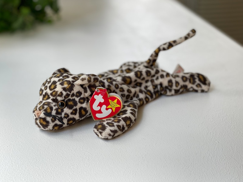 A Freckles the Spotted Leopard on a white table with a plant in the background.