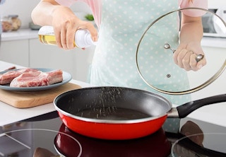 a person spraying cooking oil in a pan