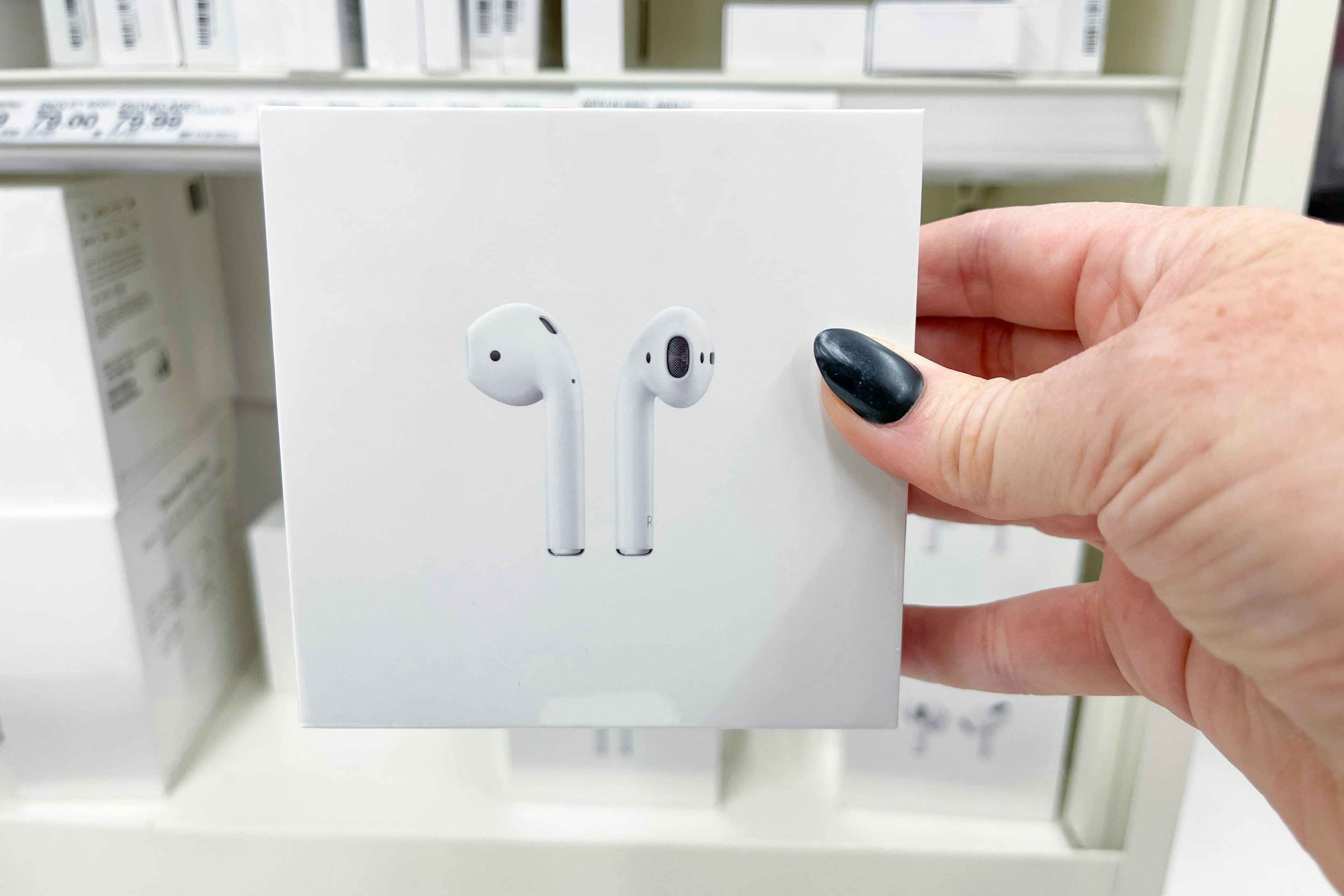 Someone holding a box of Apple Airpods in front of a shelf.