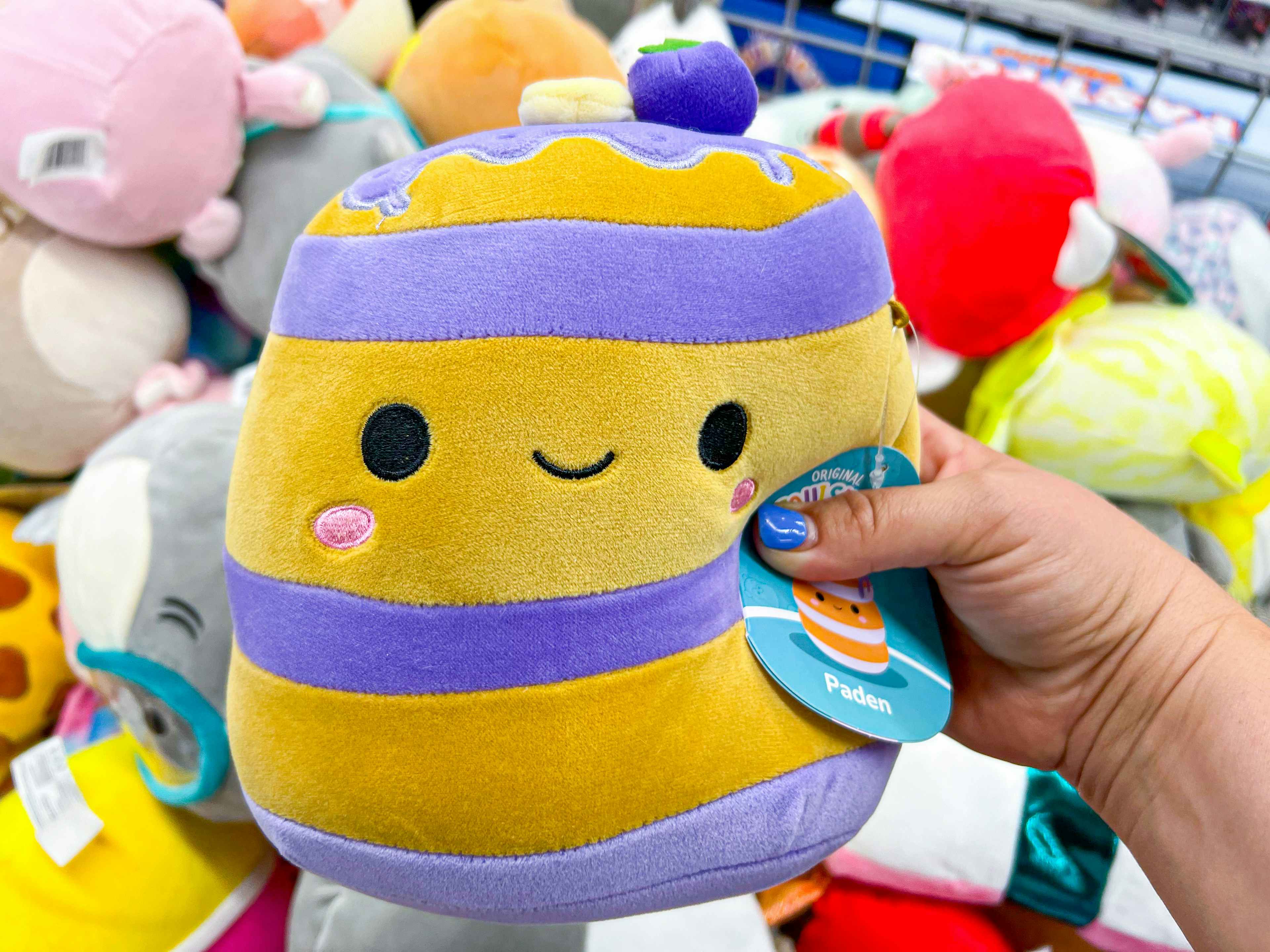 Paden the Pancake yellow and purple squishmallow toy held by a hand