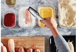 a hand with tongs putting for in food containers
