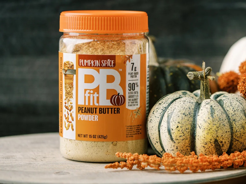 a jar of some pumpkin spice PBfit powder on a counter next to a gourd