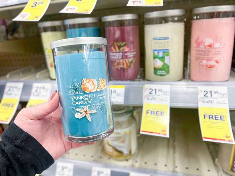 person holding a yankee candle by a buy one, get one free sign