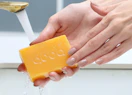 hands holding a bar of koji acid soap under a sink faucet