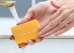 hands holding a bar of koji acid soap under a sink faucet
