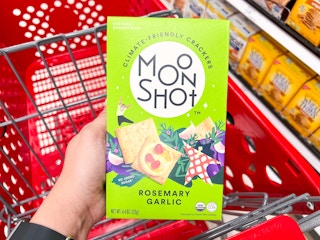 A person putting a box of moonshot crackers into a Target shopping cart