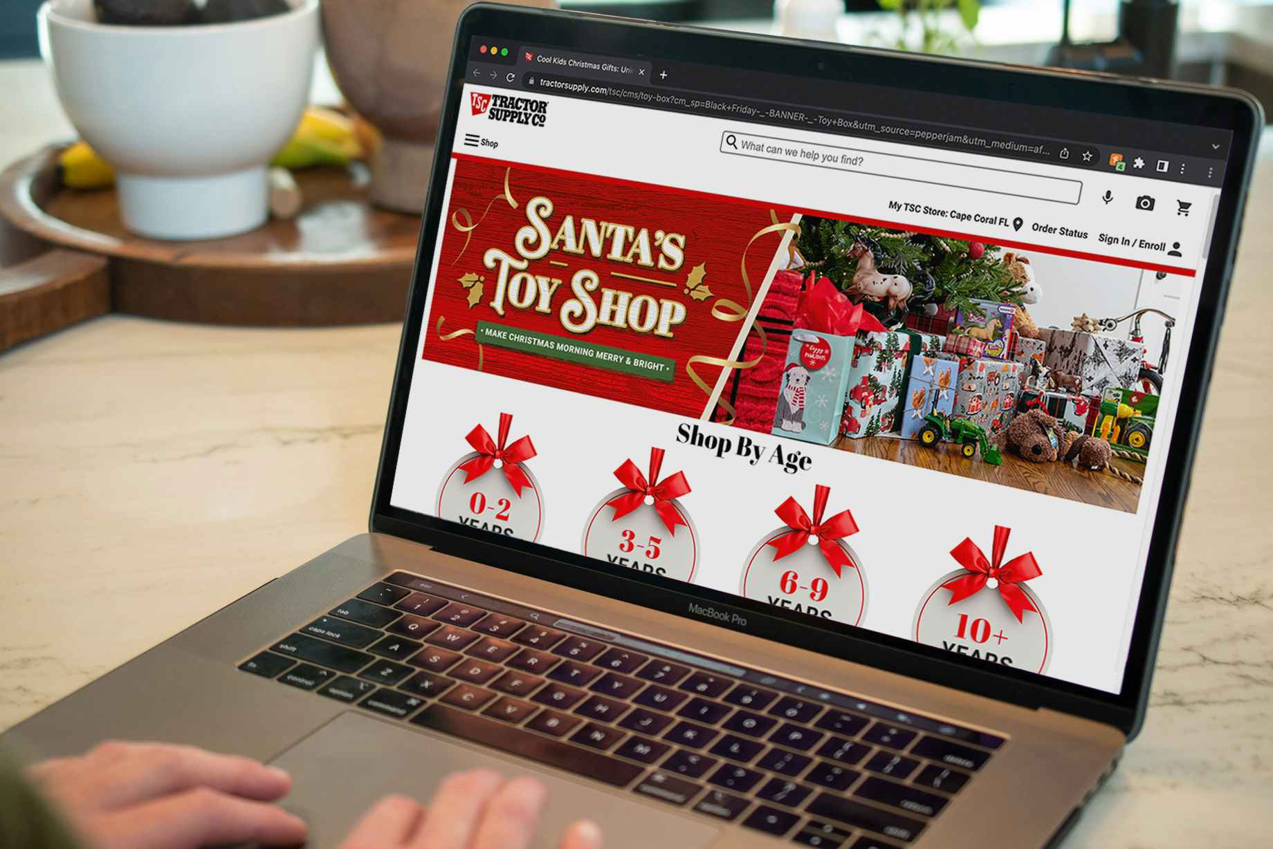 A person using a laptop displaying the Santa's Toy Shop page of the Tractor Supply Company website.