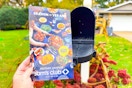 a hand holding the sam's club black friday book in front of a mail box 