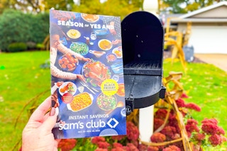 a hand holding the sam's club black friday book in front of a mail box 