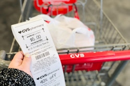 a hand holding a cvs extra bucks rewards receipt next to a cvs cart
