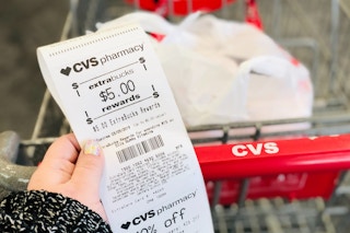 a hand holding a cvs extra bucks rewards receipt next to a cvs cart