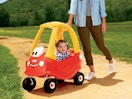 a kid in a toy car outside with a parent