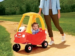 a kid in a toy car outside with a parent