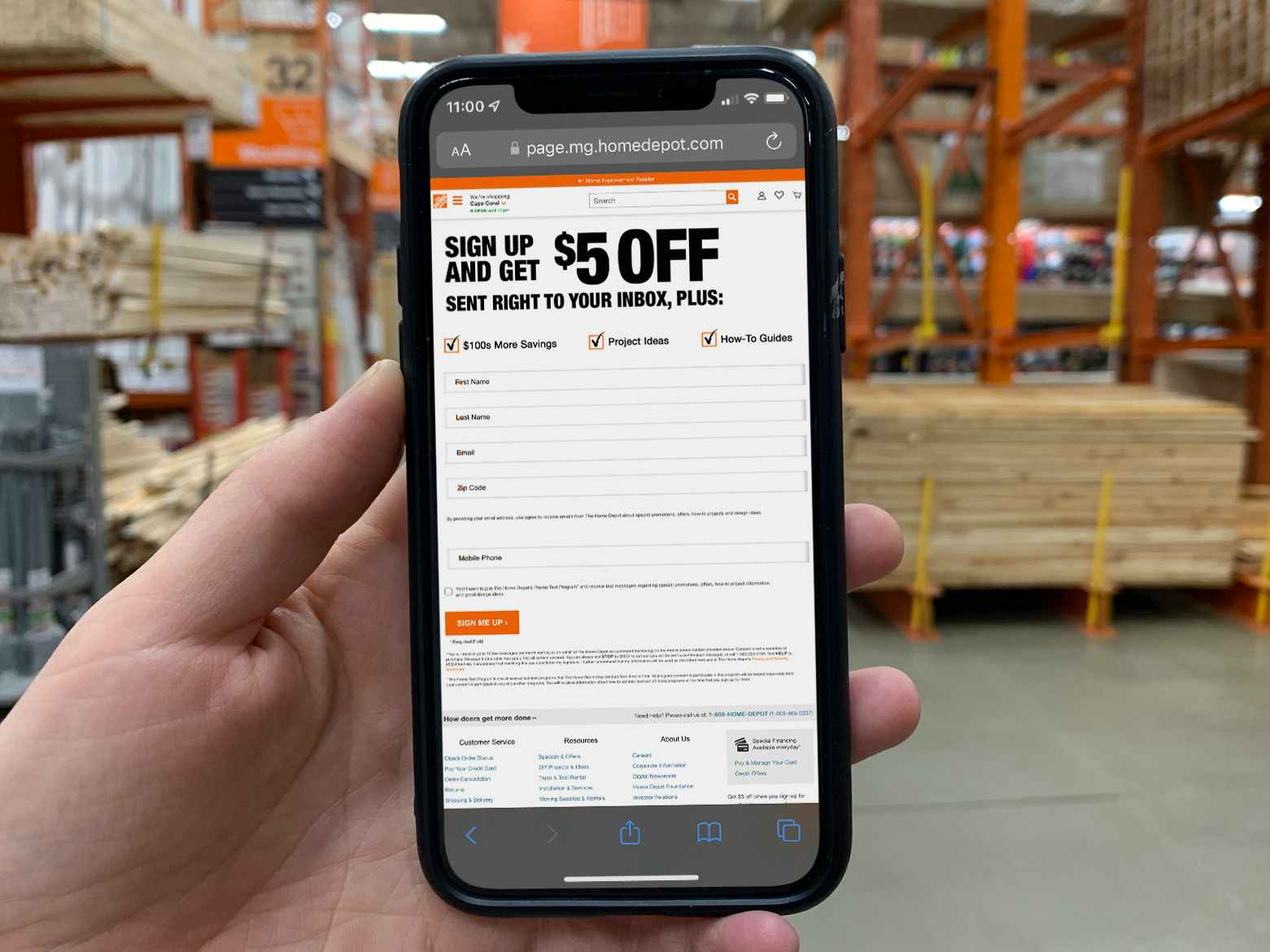 A person holding up a cell phone displaying the garden club sign up page on Home Depot's website offering a $5 off coupon