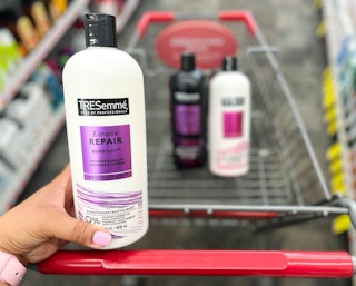 hand holding bottle of Tresemme conditioner in front of shopping cart with Tresemme shampoo and conditioner inside