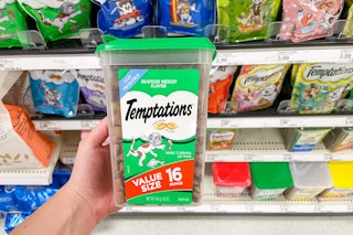 A hand holding a tub of cat treats in a store aisle