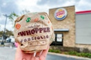 A person holding a Burger King Whopper in front of a Burger King restaurant.