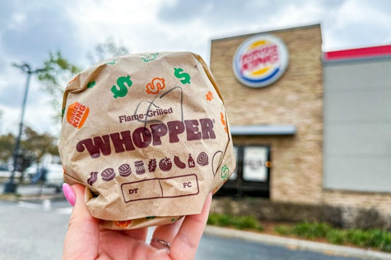 A person holding a Burger King Whopper in front of a Burger King restaurant.