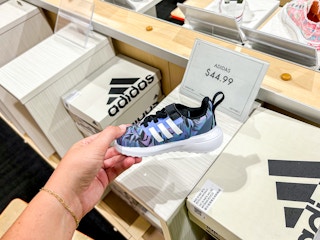 a person holding up kids adidas shoes in DSW